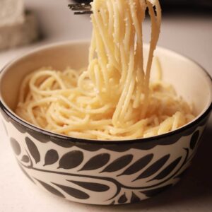 Mariposas kids buttered spaghetti noodles with Parmesan cheese in a black-and-white patterned bowl.