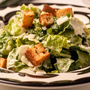 Mariposas Caesar Salad with crisp romaine, golden croutons, and shaved Parmesan in a patterned bowl.