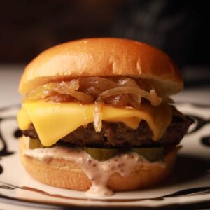 Mariposas cheeseburger with melted cheese, caramelized onions, pickles, and creamy sauce on a toasted bun.