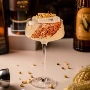 Mariposas Elotero cocktail with a chile-seasoned rim, ice, and a corn-inspired garnish in a stemmed glass.