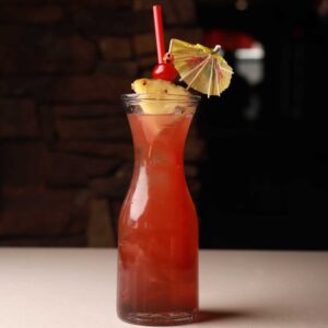 Mariposas Mai Tai, a ruby-red cocktail garnished with pineapple, cherry, a paper umbrella, and a red straw.