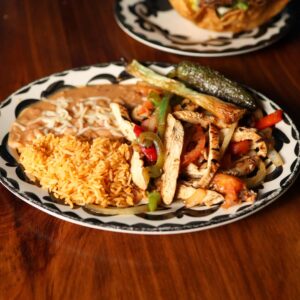 Mariposas chicken fajitas with sautéed peppers and onions, Mexican rice, refried beans, grilled onion, and a roasted jalapeño.