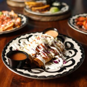 Mariposas Combination Plate with three crispy rolled tacos topped with cheese, cabbage, and crema, served with two salsas.